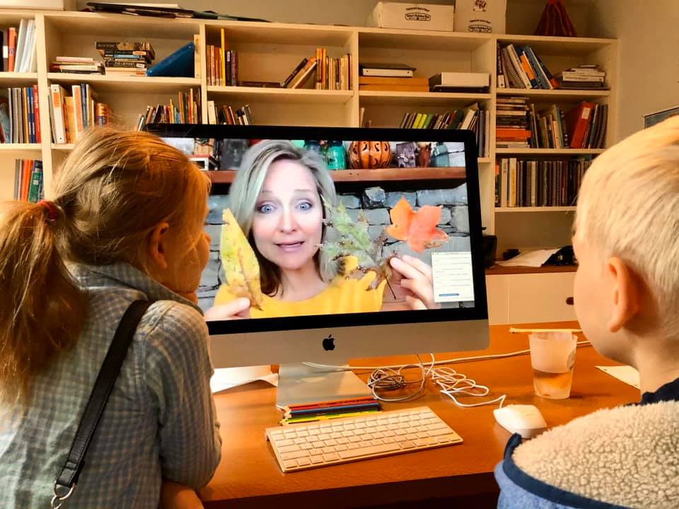 Kids watch Mrs. Cindy teach a nature study class on a computer in front of a book case filled with books.