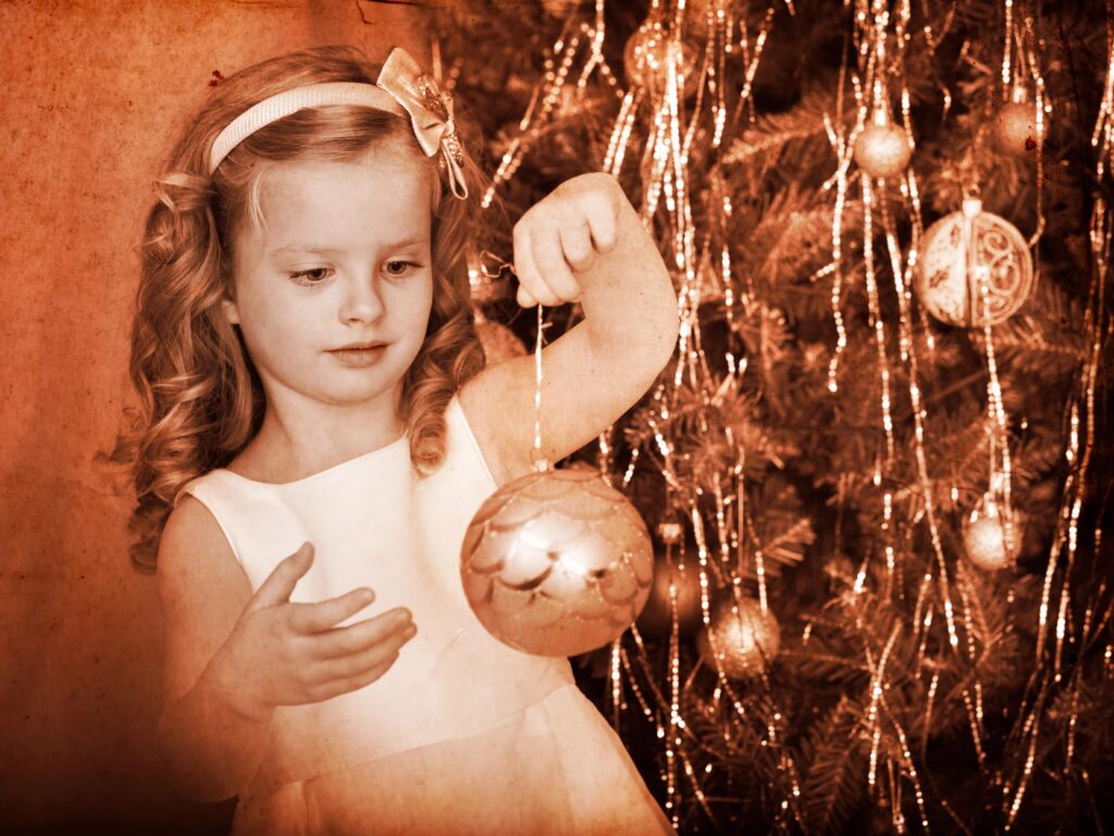 little girl with a ball ornament sitting in front of a Christmas tree
