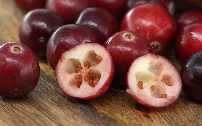 red cranberries with one cut in half on a wooden table